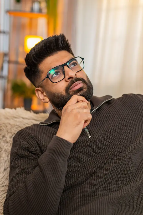 indian-young-man-sofa-home-looks-side-nostalgic-face-thinking-someone-dear-sits-gazes-out-dreamy-expression-394889989